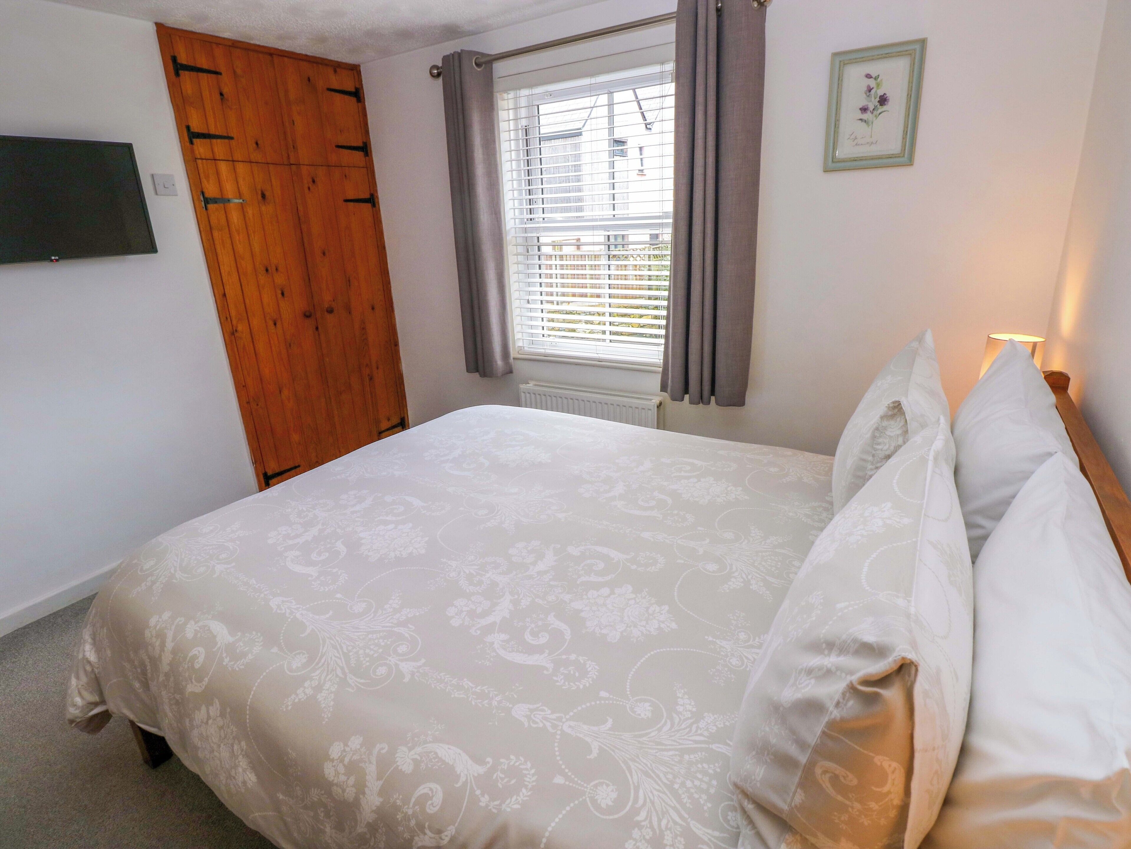 A bedroom with a bed, a wooden wardrobe, a window with curtains, and a framed picture on the wall.