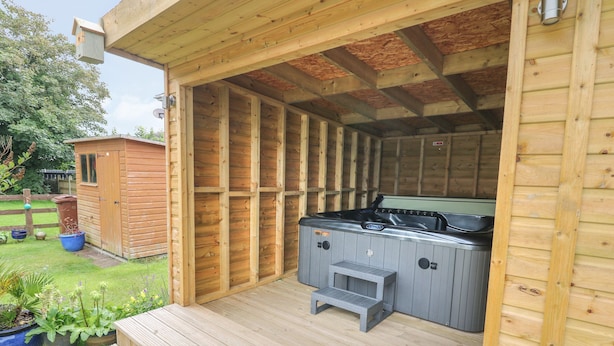 A wooden outdoor hot tub area with steps leading up to it, surrounded by a wooden deck and a garden. - 4 Ty Rhosyn (Porthmadog)