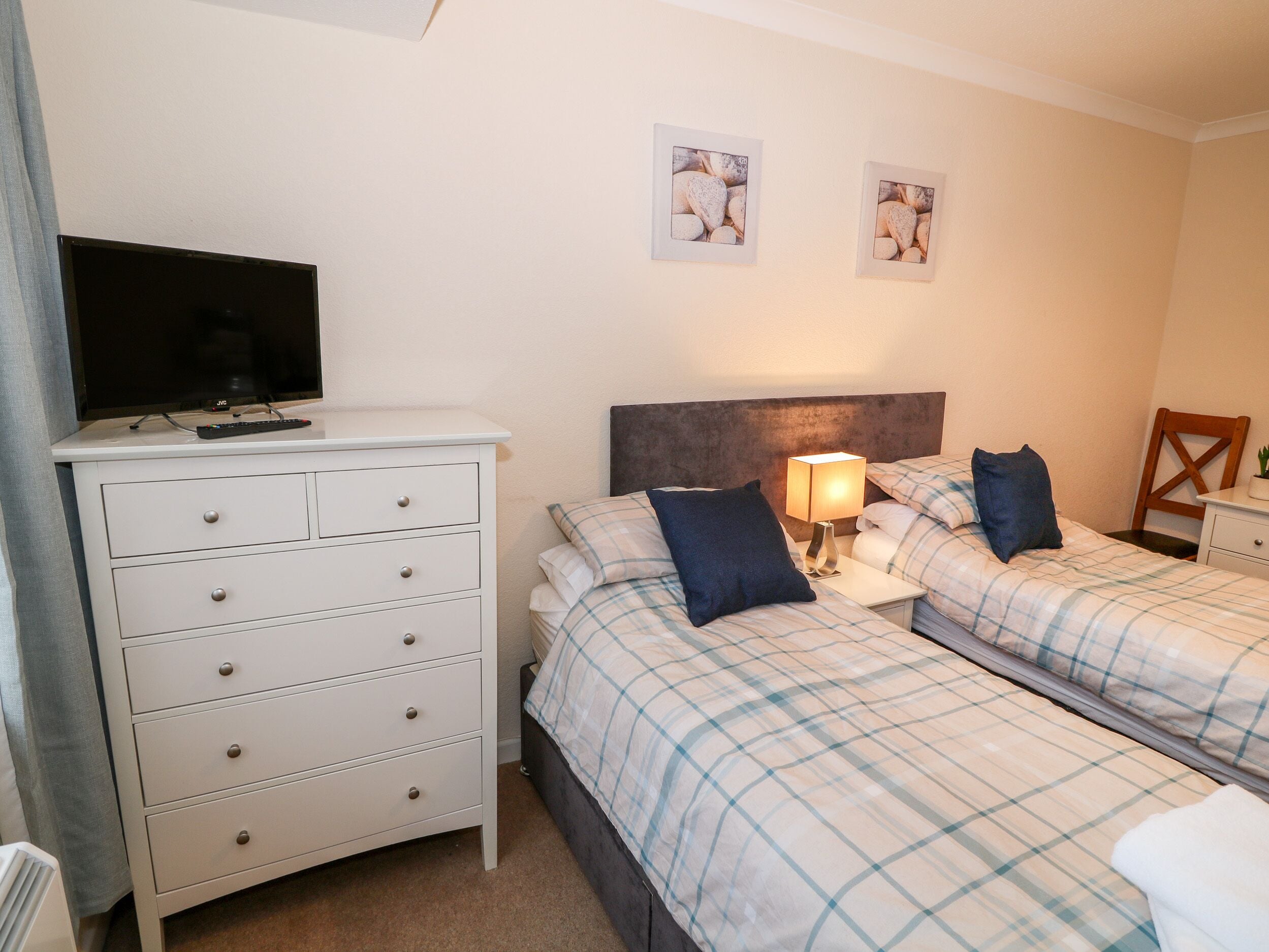 A hotel room with a bed, a dresser, a TV, and two framed pictures on the wall.