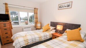 A bedroom with two beds, a dresser, a television, and a window with curtains. - 4 Ty Rhosyn (Porthmadog)