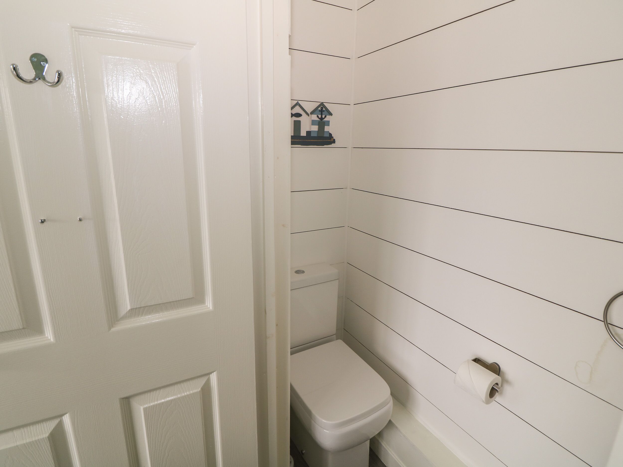 A bathroom with white walls, a white door, a toilet, and a small shelf with a house decoration.