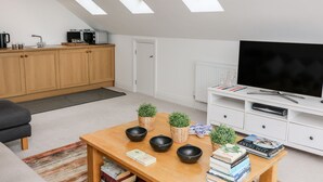 A modern living room with a flat-screen TV, wooden furniture, and skylights. - St Julien (Dawlish)