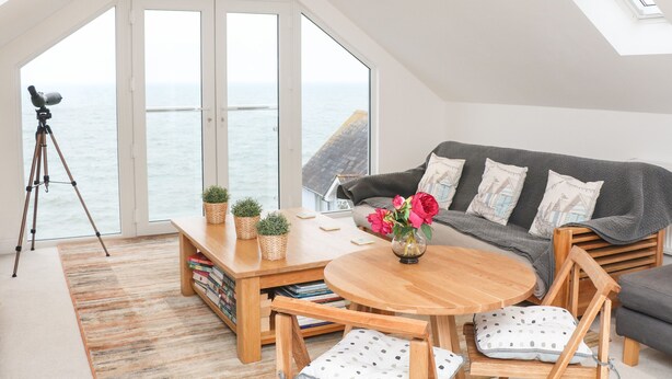 A cozy living room with a view of the sea, a telescope, and a wooden coffee table with books and plants. - St Julien (Dawlish)
