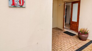 A building entrance with a number plaque, a wooden door, a potted plant, and a tiled floor. - St Julien (Dawlish)