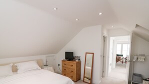 A bedroom with a large bed, a dresser, a television, and a mirror. There is a door leading to another room. - St Julien (Dawlish)