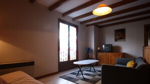 A living room with a sofa, a table, a television, and a window with curtains. - Family-Friendly Countryside Cottage with Modern Amenities, Near Thermal Baths and Nature Spots (Le Val-d'Ajol)