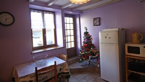 A kitchen with a dining table, chairs, a refrigerator, a microwave, a Christmas tree, and a window with curtains. - Family-Friendly Countryside Cottage with Modern Amenities, Near Thermal Baths and Nature Spots (Le Val-d'Ajol)