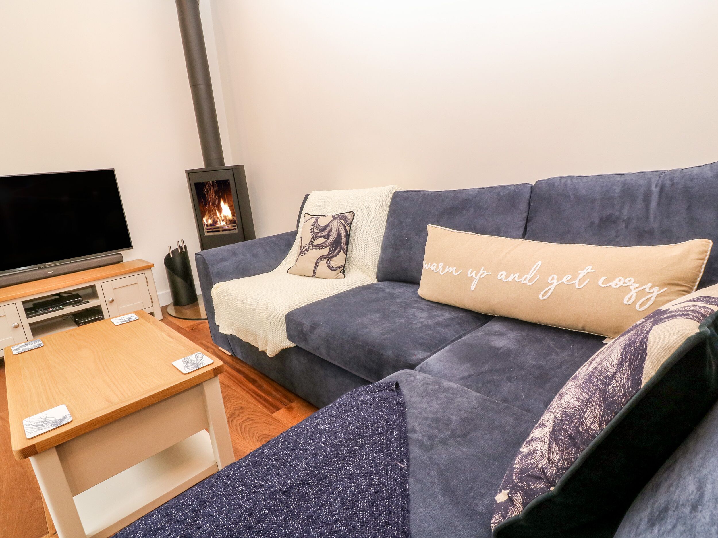 Ein gemütliches Wohnzimmer mit einem dunkelblauen Sofa, einem Flachbildfernseher, einem kleinen Holztisch und einem Kamin.