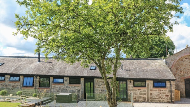 A stone building with multiple windows and a tree in front. - Nana's Cottage (Camborne)