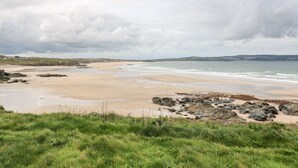 A coastal landscape with a sandy beach, rocky outcrops, and grassy areas. - Nana's Cottage (Camborne)