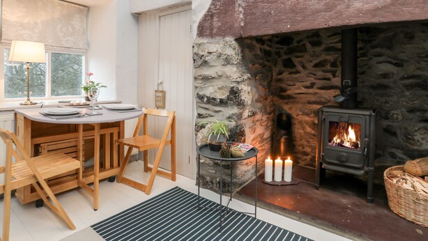 A cozy room with a stone fireplace, a dining table with chairs, and a small side table with candles. - Y Garreg Fawr (Caernarfon)