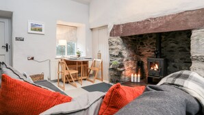 A cozy living room with a stone fireplace, a dining area with a table and chairs, and a view of the outdoors through a window. - Y Garreg Fawr (Caernarfon)