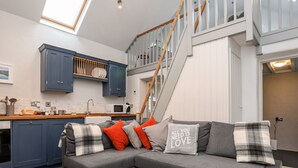 A modern kitchen with dark blue cabinets, a wooden countertop, and a built-in microwave. - Y Garreg Fawr (Caernarfon)