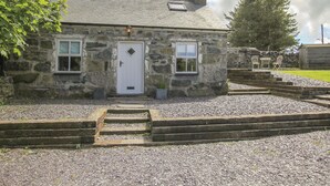 A stone cottage with a white door, two windows, and a small porch. - Y Garreg Fawr (Caernarfon)