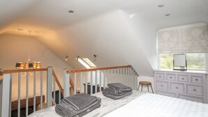 A bedroom with a sloped ceiling, a wooden staircase, a bed with white bedding, a dresser with drawers, and a window with a view. - Y Garreg Fawr (Caernarfon)