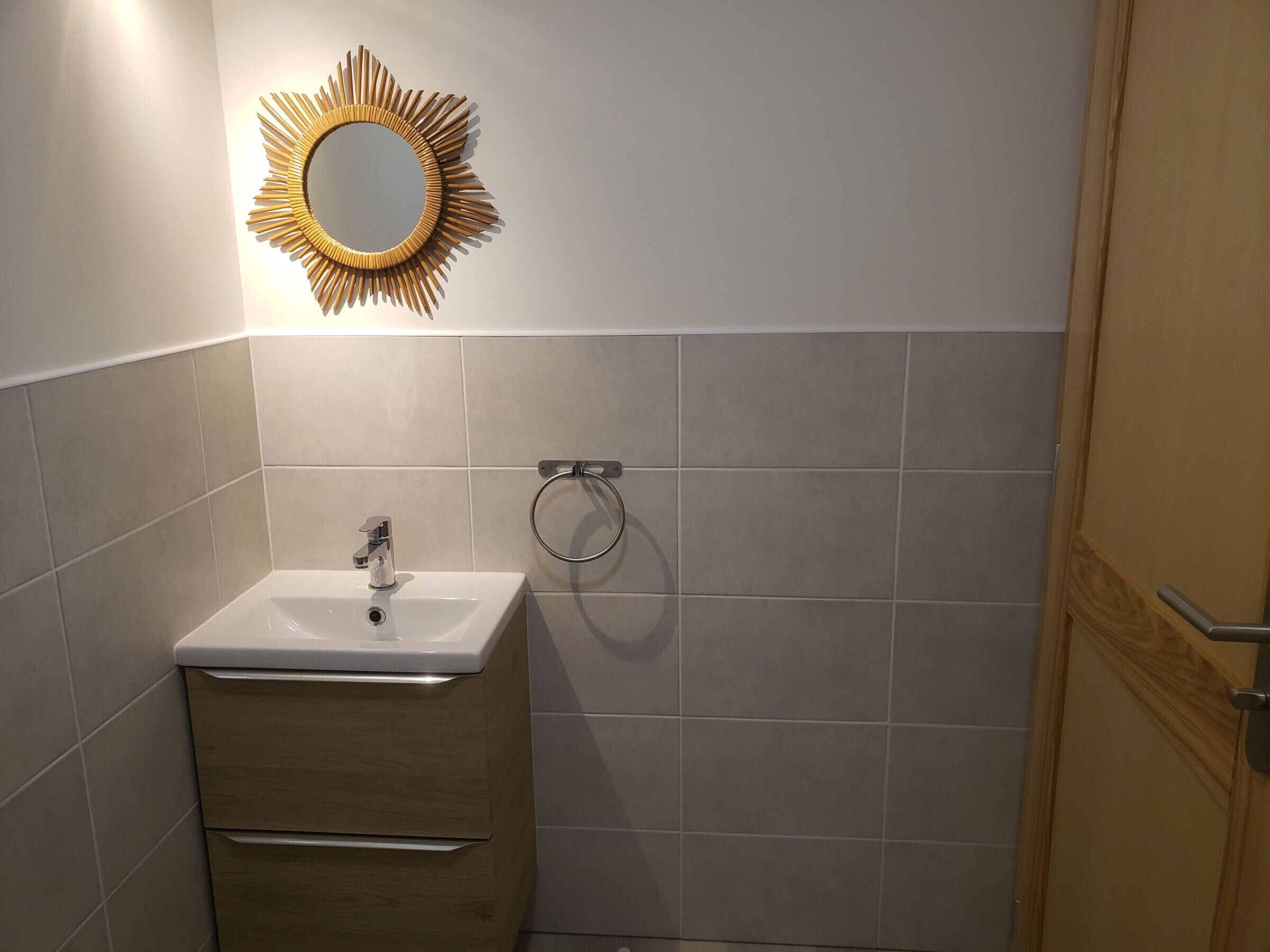 Une salle de bain avec un lavabo blanc, un meuble en bois et un miroir en forme de soleil.