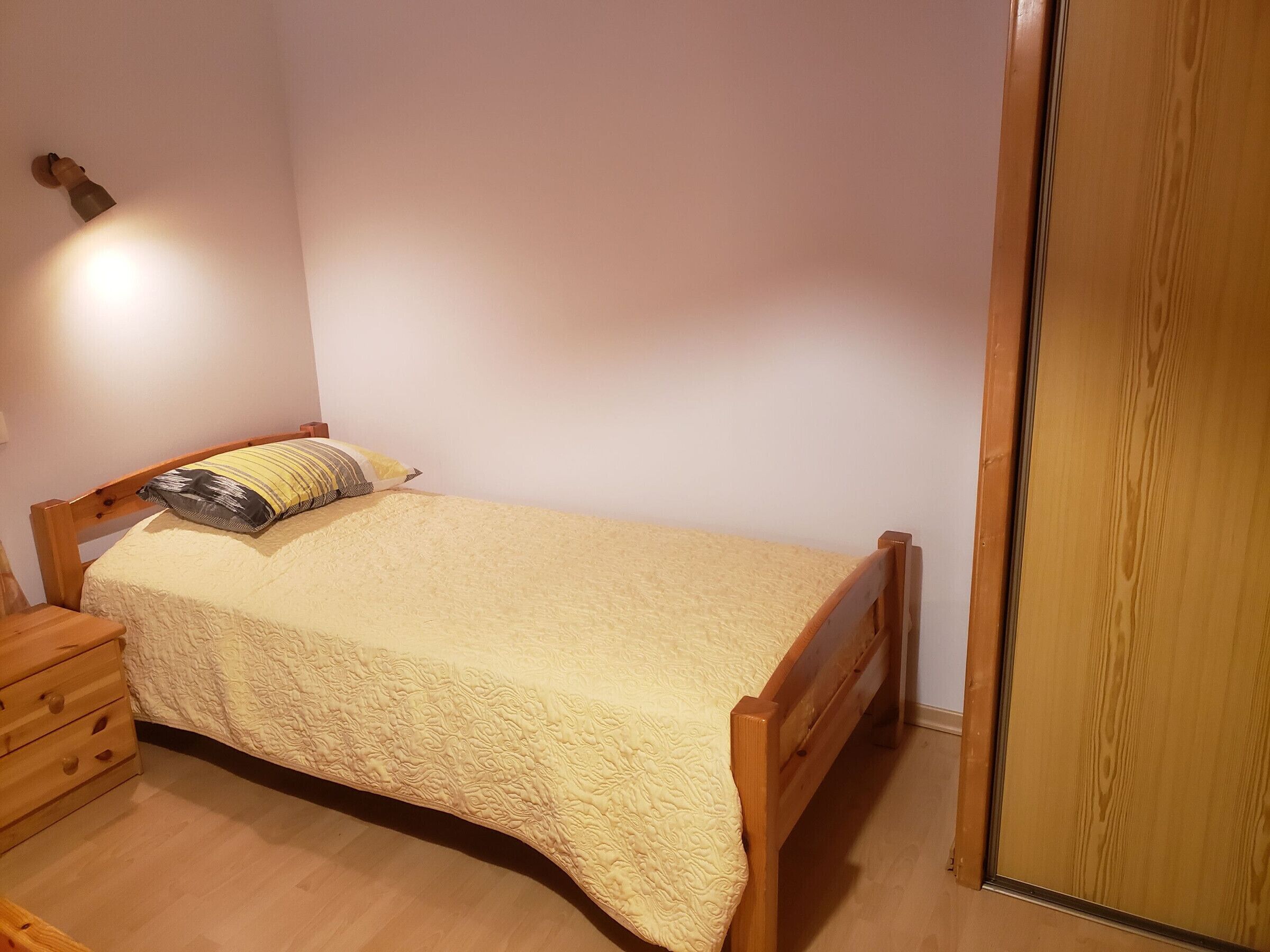 A single bed with a wooden frame and a textured bedspread, a nightstand with a lamp, and a wooden wardrobe.