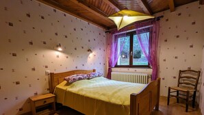 A bedroom with a wooden bed, a nightstand, a chair, a window with curtains, and a radiator. - Cozy Mountain Retreat with Garage, BBQ & Wifi in La Bresse (La Bresse)