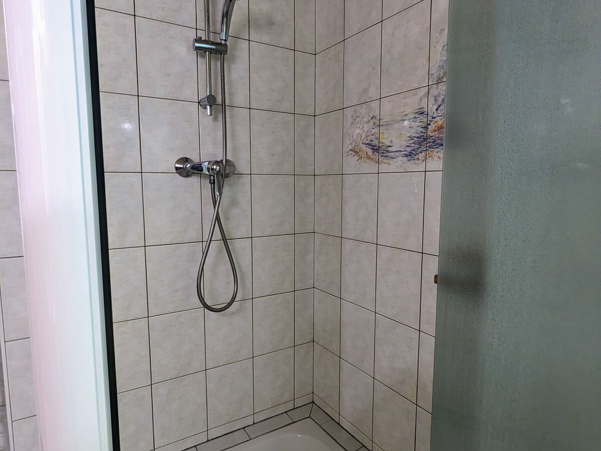 Eine Eckdusche mit Handbrause und Wandarmatur.