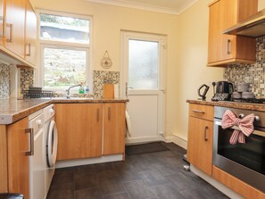 A kitchen with wooden cabinets, a washing machine, a coffee maker, and a tiled backsplash.