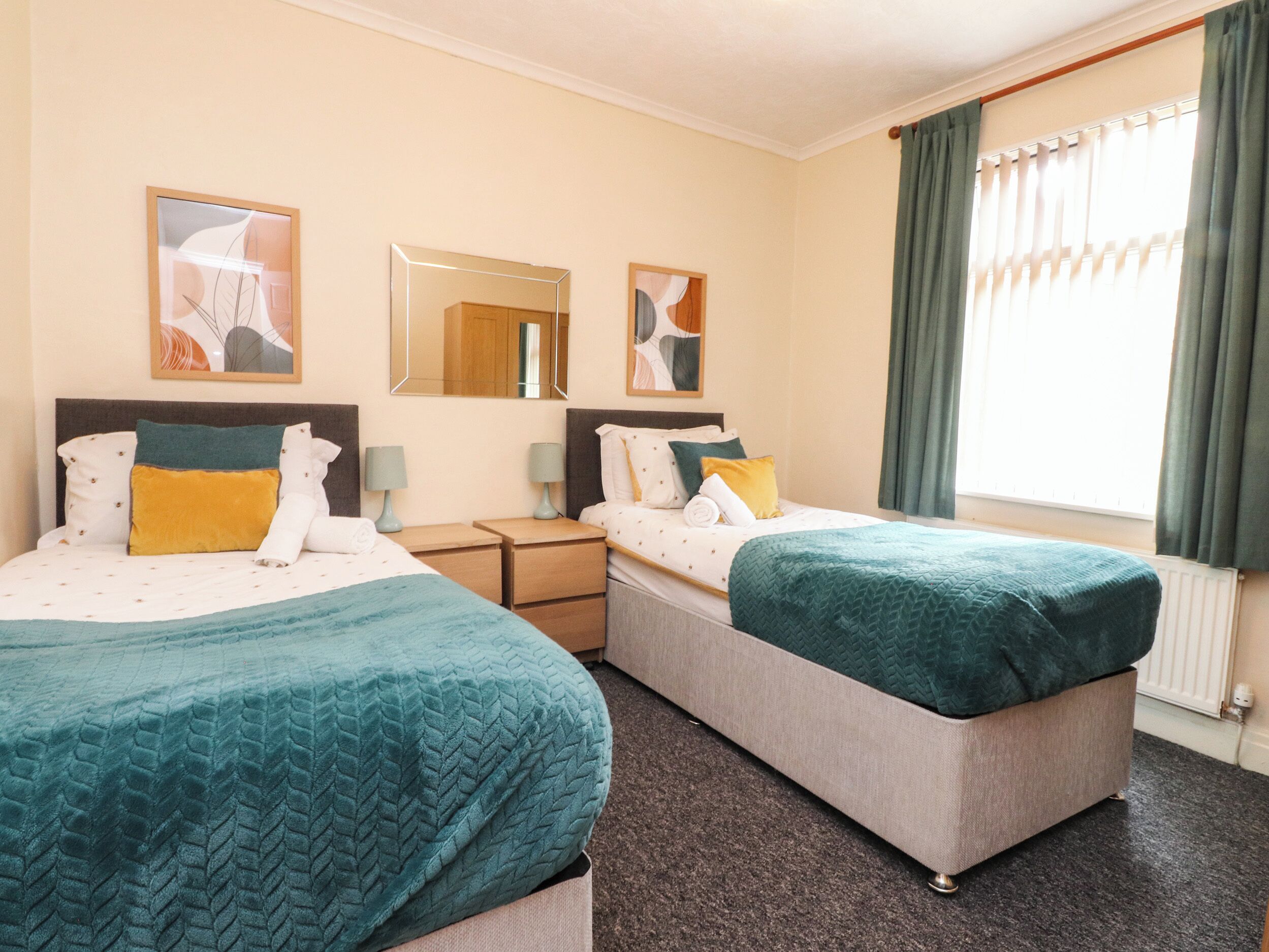 A hotel room with two beds, a large mirror, and a window with curtains.