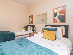 Una habitación de hotel con dos camas, cada una con un edredón de diferente color, una mesita de noche con lámpara y obras de arte en las paredes.