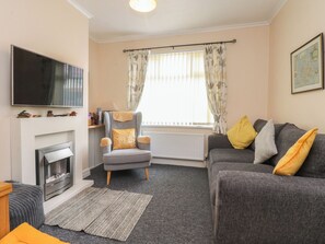 A living room with a fireplace, a grey armchair, a grey sofa, and a television. - Cosy Bee (Morecambe)