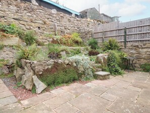 Un muro de piedra con un área ajardinada, una valla de madera y un sendero de piedra.