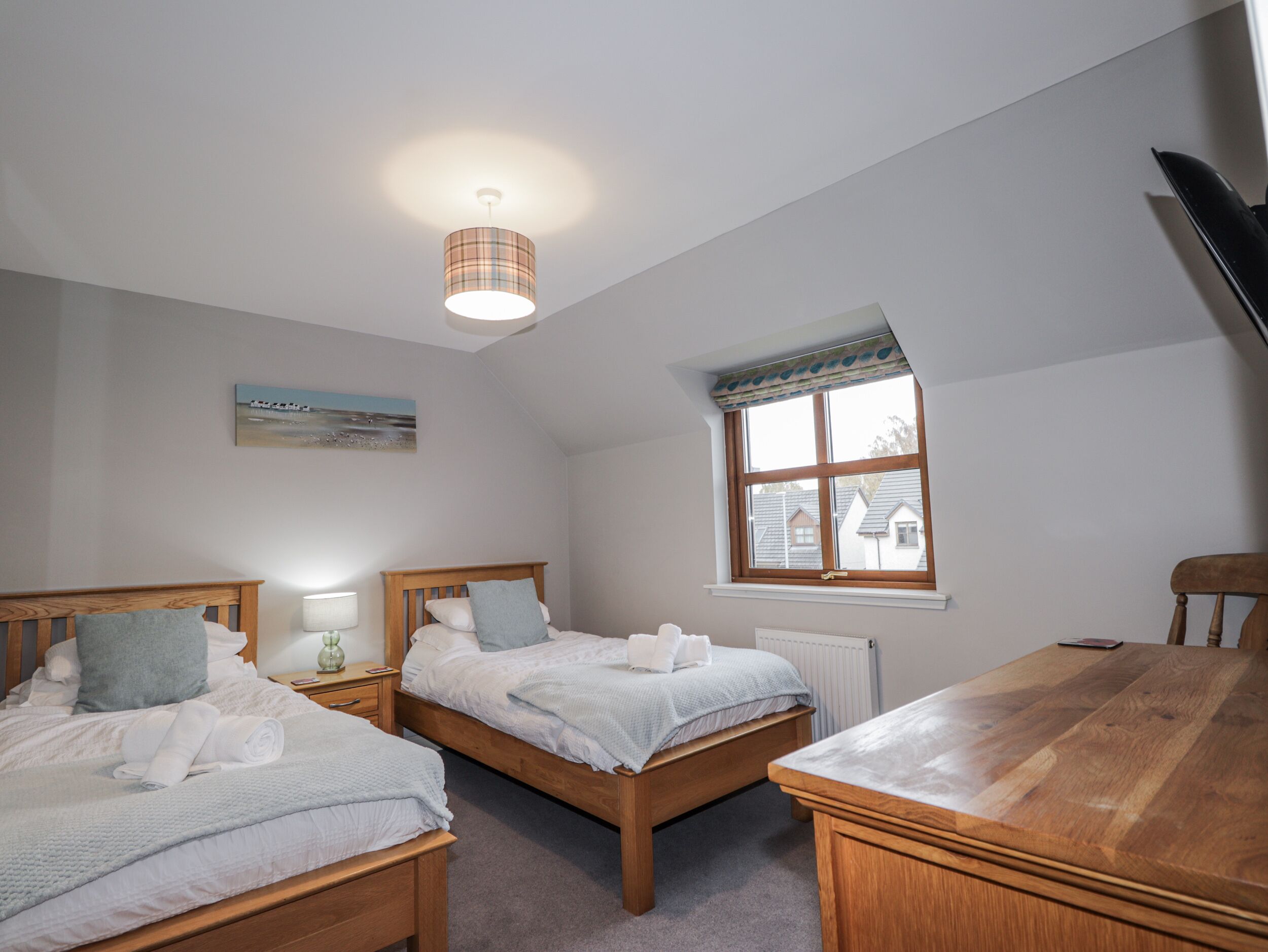 A bedroom with two wooden beds, a wooden table, a window with a view, and a ceiling light.