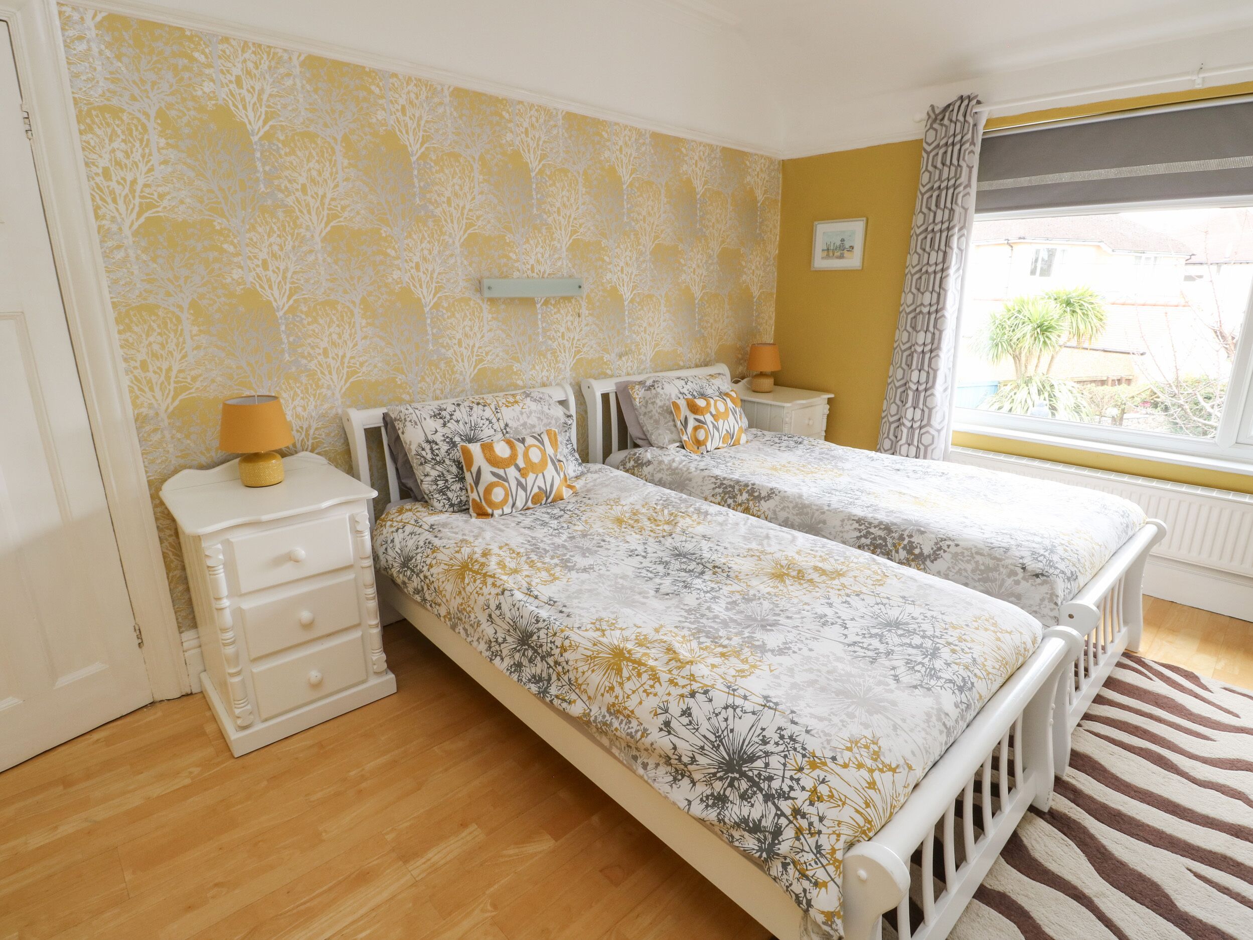 A bedroom with two beds, a nightstand, a dresser, and a window with a view of the outside.