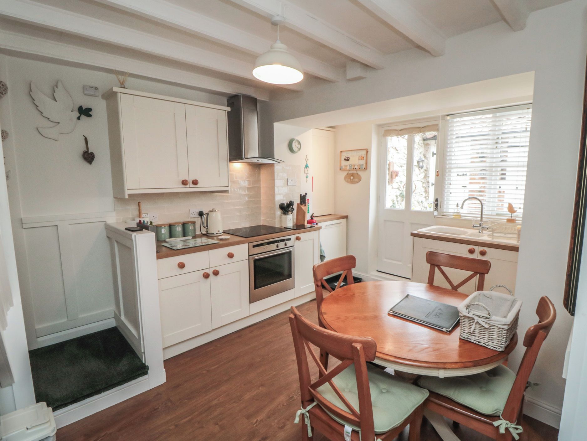 A compact kitchen with white cabinetry, a built-in oven, and a dining area with a wooden table and chairs.