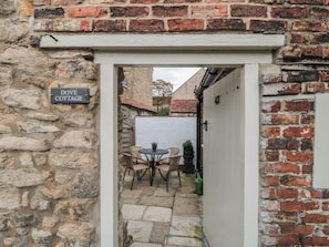 A stone cottage entrance with a sign reading 'DOVE COTTAGE,' a small patio with a table and chairs, and a white door. - Dove Cottage (Pickering)