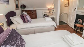 A hotel room with two beds, a dresser, a vanity with a mirror, and a fireplace. - Dove Cottage (Pickering)