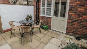 A patio with a round table and two wicker chairs, a white door, and a brick wall. - Dove Cottage (Pickering)