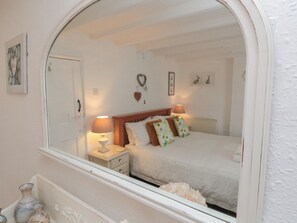 A bedroom with a large arched mirror, a wooden headboard, a bedside table with a lamp, and a radiator. - Dove Cottage (Pickering)