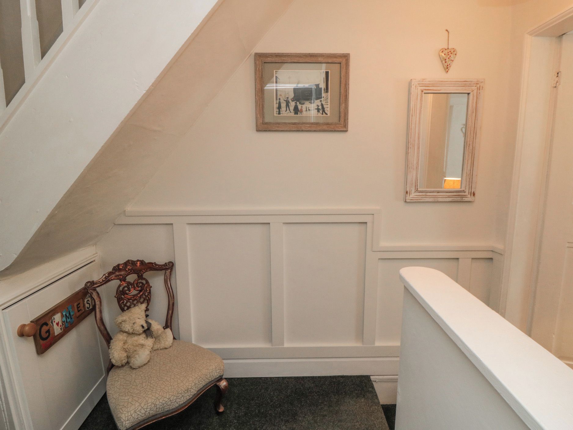 A staircase with a white railing, a chair with a teddy bear, and a wall with a framed picture and a mirror.