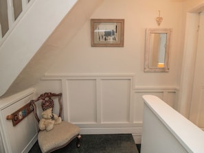 Una escalera con barandilla blanca, una silla con un osito de peluche, y una pared con un cuadro enmarcado y un espejo.