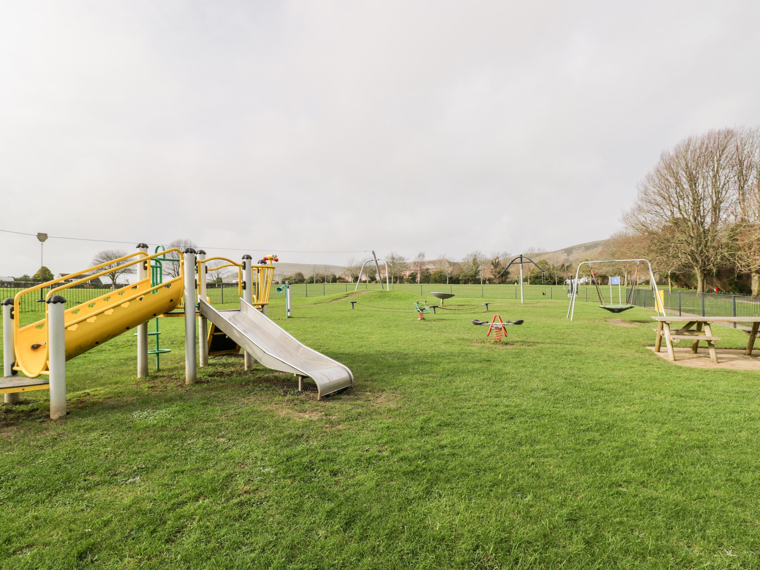 Un parque infantil con un tobogán amarillo y columpios.