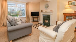 A living room with a fireplace, a sofa, a television, and a window with curtains. - Westholme (Barnard Castle)