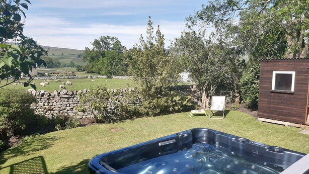 A hot tub in a backyard with a stone wall, a wooden cabin, and a grassy field with sheep in the background. - Westholme (Barnard Castle)