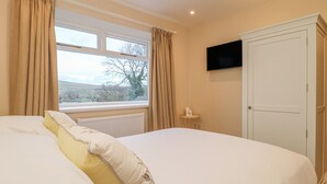A bedroom with a bed, a window with curtains, a radiator, a television on the wall, and a wardrobe. - Westholme (Barnard Castle)
