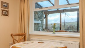 A dining area with a table set for two, a window with a view of the countryside, and a stone wall behind the window. - Westholme (Barnard Castle)