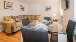 A modern living room with a glass dining table, a sofa set, and a flat-screen TV mounted on the wall. - Midships (St Austell)
