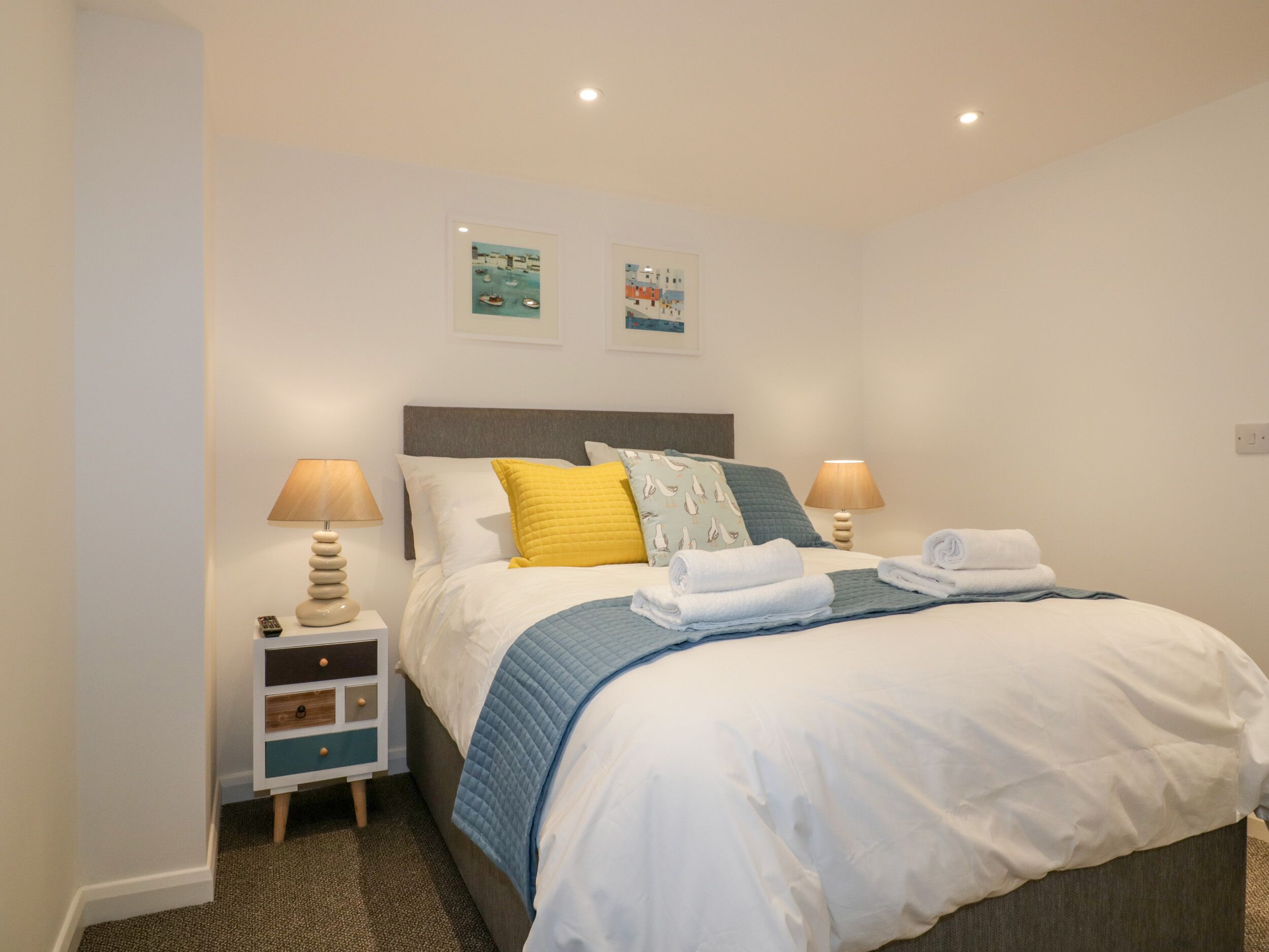 A neatly made bed with white and blue bedding, two bedside lamps, and a small bedside table with a lamp and a remote control.