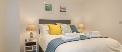 A neatly made bed with white and blue bedding, two bedside lamps, and a small bedside table with a lamp and a remote control.