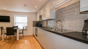 A modern kitchen with a built-in oven, a stainless steel sink, and a coffee maker. - Midships (St Austell)