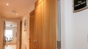 A hallway with wooden doors, a sign reading "The Crows Nest," and a view into a room with a window and a table. - The Crows Nest (St Austell)