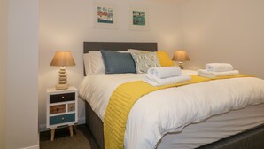 A neatly made bed with white and yellow bedding, two pillows, and folded towels on a bedside table. - The Crows Nest (St Austell)