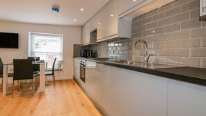 A modern kitchen with a built-in island, stainless steel appliances, and grey subway tiles. - The Crows Nest (St Austell)