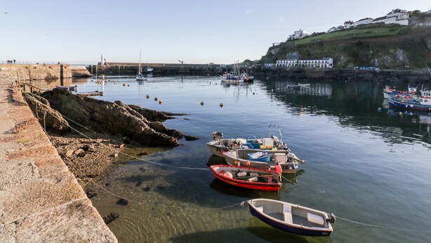 A harbor with boats docked, a stone quay, and a lighthouse in the background. - The Crows Nest (St Austell)